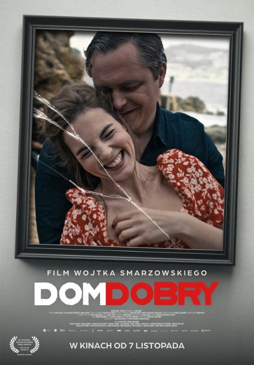 Plakat filmu „Dom dobry” w reżyserii Wojciecha Smarzowskiego. Na plakacie widoczny jest portret mężczyzny i kobiety w średnim wieku, uśmiechających się do siebie. Ich twarze są częściowo ukryte za ramą zdjęcia, która jest pęknięta wzdłuż linii ich twarzy, co sugeruje kryzys w ich relacji. Tło jest rozmyte, co podkreśla intymność i napięcie emocjonalne. U góry plakatu duży, czerwony napis „DOM DOBRY”, poniżej mniejszymi literami „Wojciech Smarzowski”. Całość utrzymana w stonowanej kolorystyce, z dominującymi odcieniami czerwieni i czerni.
