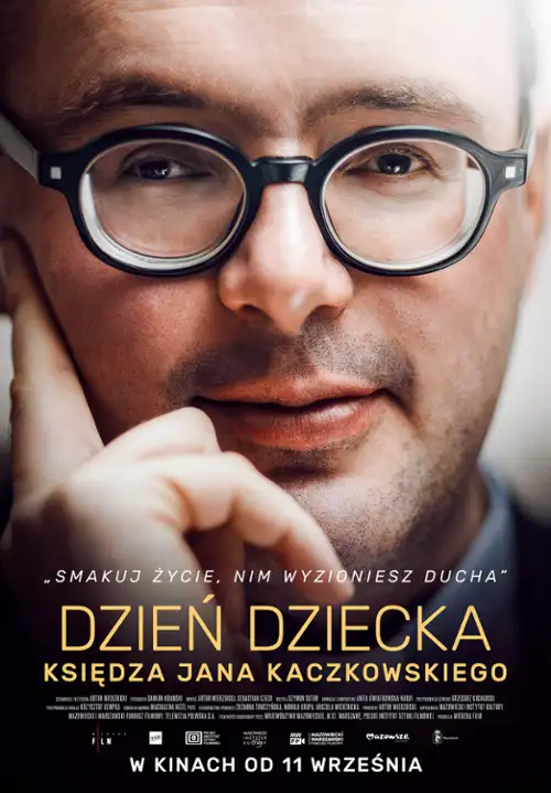 Plakat przedstawia zbliżenie twarzy mężczyzny w okularach, który patrzy prosto w stronę widza. Mężczyzna ma krótkie włosy, zarost i ubrany jest w ciemną koszulę lub marynarkę. Jedną ręką opiera twarz na policzku. Tło jest jasne w górnej części i stopniowo przechodzi w ciemne, niemal czarne. Nad tytułem umieszczono hasło: „SMAKUJ ŻYCIE, NIM WYZIĘNIESZ DUCHA”. W centralnej części plakatu znajduje się tytuł filmu: „DZIEŃ DZIECKA KSIĘDZA JANA KACZKOWSKIEGO”, zapisany dużymi, złotymi literami. Na dole znajduje się drobny tekst informacyjny oraz informacja: „W KINACH OD 11 WRZEŚNIA”.