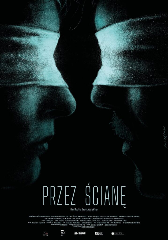 Pionowy plakat utrzymany w ciemnej, niemal czarnej kolorystyce z turkusowo-niebieskim światłem. W górnej i środkowej części widzimy zbliżenia dwóch ludzkich twarzy, przedstawionych z profilu. Po lewej stronie znajduje się twarz mężczyzny zwróconego w prawo, a po prawej twarz drugiego mężczyzny, zwróconego w lewo. Ich nosy niemal się stykają, ale między nimi pozostaje wąska, czarna przestrzeń. Obaj mają zamknięte oczy lub oczy przysłonięte cieniem, a ich twarze są oświetlone chłodnym, turkusowym światłem. Wyraźnie widoczne są nosy, usta i fragmenty policzków. Pomiędzy twarzami dominuje głęboka czerń, podkreślająca wrażenie oddzielenia i napięcia. W dolnej części plakatu, na czarnym tle, umieszczono duży, jasnoturkusowy tytuł zapisany wąskimi, wysokimi literami: „PRZEZ ŚCIANĘ”. Bezpośrednio pod nim znajduje się niewielki napis: „film Macieja Sobieszczańskiego”. Przy dolnej krawędzi widnieją drobne napisy informujące o twórcach i producentach filmu oraz logotypy instytucji zaangażowanych w jego powstanie. Całość jest minimalistyczna, surowa i niepokojąca. Zbliżenie twarzy oraz niemal całkowicie czarne tło budują wrażenie bliskości, która jednocześnie nie pozwala na pełne spotkanie.